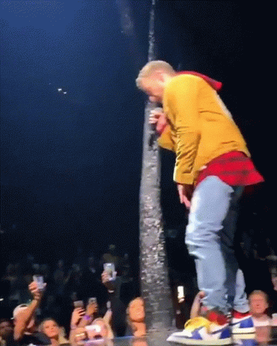 A Man In A Yellow Jacket Is Singing Into A Microphone While Standing On A Stage GIF