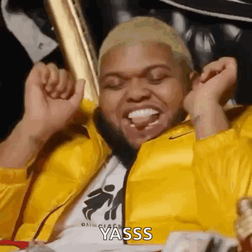 A Man In A Yellow Jacket Is Sitting In A Chair With His Hands In The Air And The Word Yasss Written On The Bottom GIF