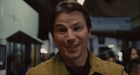 A Man In A Yellow Jacket Is Smiling In A Crowded Room GIF