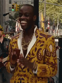 A Man In A Yellow Jacket Is Smiling In Front Of A Green Light GIF