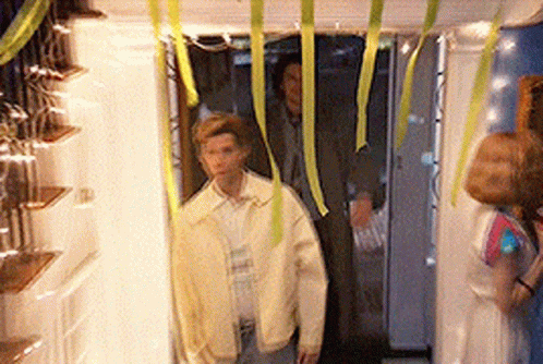 A Man In A Yellow Jacket Is Standing In A Hallway With Ribbons Hanging From The Ceiling GIF