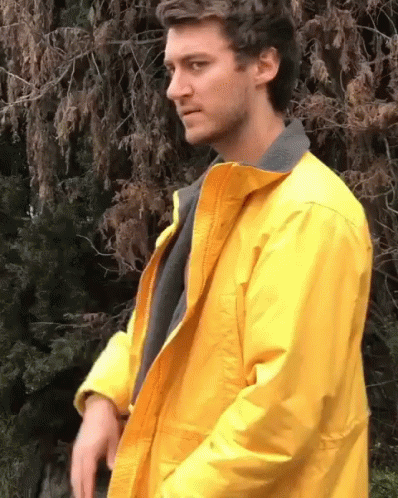 A Man In A Yellow Jacket Is Standing In Front Of A Tree GIF