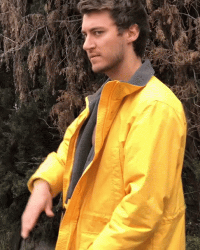 A Man In A Yellow Jacket Is Standing In Front Of Trees GIF