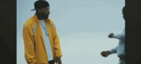 A Man In A Yellow Jacket Is Standing Next To Another Man In A Blue Shirt . GIF