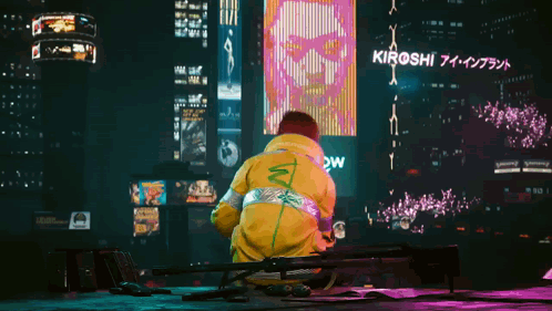 A Man In A Yellow Jacket Stands In Front Of A Large Billboard That Says Kiroshi GIF