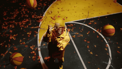 A Man In A Yellow Jacket Stands On A Basketball Court Surrounded By Basketballs And Leaves GIF