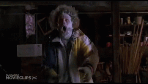 A Man In A Yellow Jacket With A Mask On His Face Is Standing In A Room . GIF