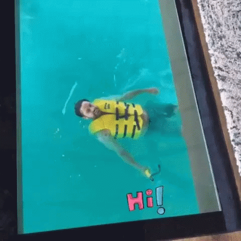 A Man In A Yellow Life Jacket Is Swimming In A Pool With The Word Hi On The Screen . GIF