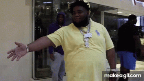 A Man In A Yellow Polo Shirt Is Standing In Front Of A Store Window With His Arms Outstretched . GIF