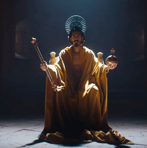 A Man In A Yellow Robe Is Holding A Crown And A Sword GIF
