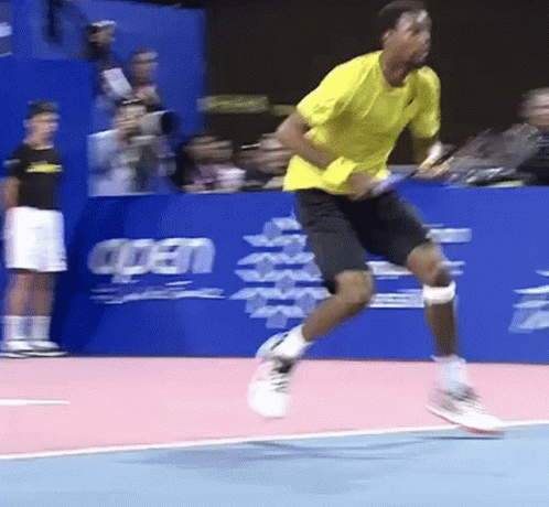 A Man In A Yellow Shirt And Black Shorts Is Jumping In The Air GIF