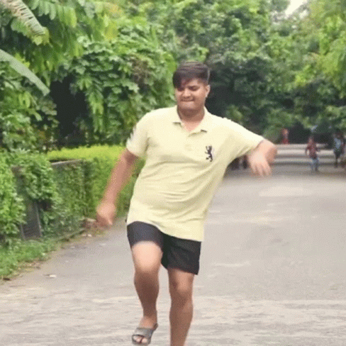 A Man In A Yellow Shirt And Black Shorts Is Running Down The Street GIF