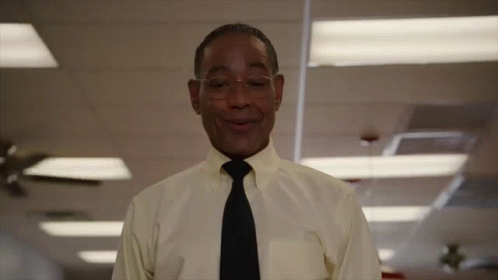 A Man In A Yellow Shirt And Black Tie Smiles GIF