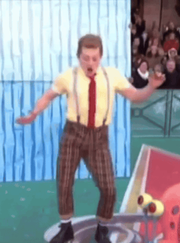A Man In A Yellow Shirt And Brown Pants Is Standing On A Platform GIF