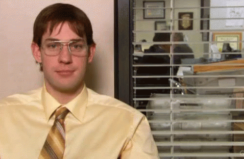 A Man In A Yellow Shirt And Tie Is Standing In Front Of A Window With Blinds . GIF