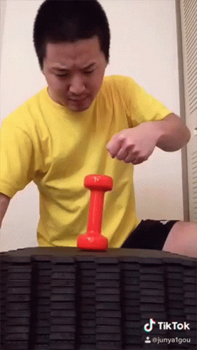 A Man In A Yellow Shirt Holds A Red Dumbbell On A Tire GIF