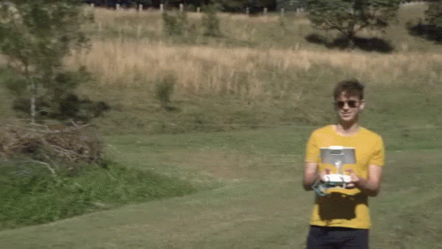 A Man In A Yellow Shirt Holds A Remote Control In His Hands GIF