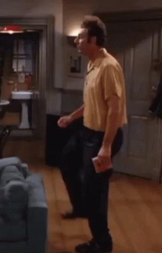 A Man In A Yellow Shirt Is Dancing In A Living Room With A Blue Couch . GIF