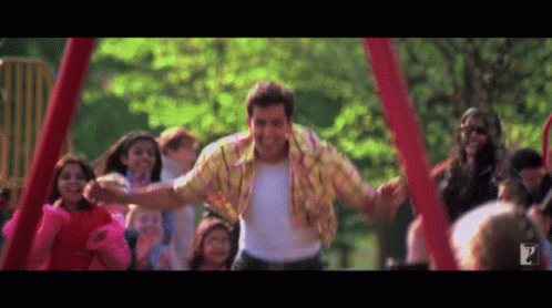 A Man In A Yellow Shirt Is Dancing In Front Of A Crowd Of Children GIF
