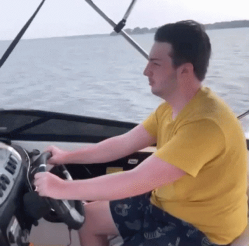 A Man In A Yellow Shirt Is Driving A Boat In The Ocean GIF