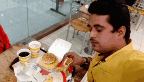A Man In A Yellow Shirt Is Eating A Mcdonald 'S Burger GIF