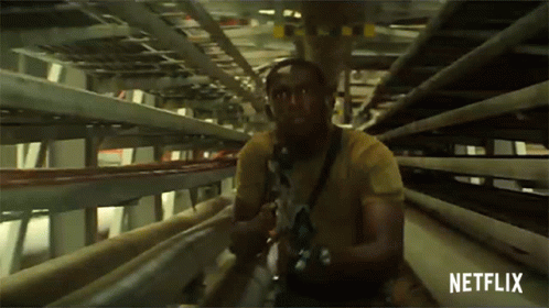 A Man In A Yellow Shirt Is Holding A Gun In A Tunnel With Netflix Written On The Bottom GIF