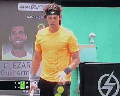 A Man In A Yellow Shirt Is Holding A Tennis Racquet In Front Of A Scoreboard That Says Clezar Guilherme GIF