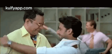 A Man In A Yellow Shirt Is Hugging Another Man In A Room . GIF