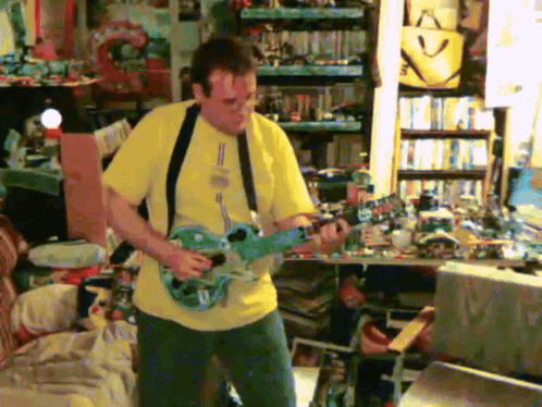 A Man In A Yellow Shirt Is Playing A Blue Guitar GIF