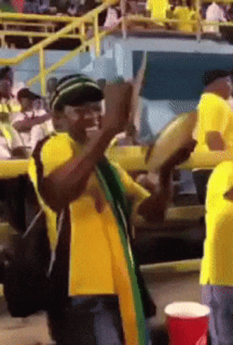 A Man In A Yellow Shirt Is Playing A Drum In A Crowd GIF
