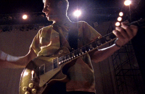 a man in a yellow shirt is playing a guitar in a dark room