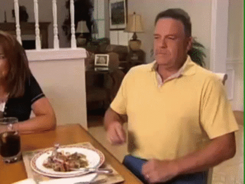 A Man In A Yellow Shirt Is Sitting At A Table With Plates Of Food On It GIF