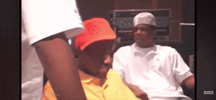 A Man In A Yellow Shirt Is Sitting Next To Another Man In A Red Hat . GIF