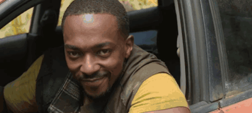 A Man In A Yellow Shirt Is Smiling While Sitting In A Car GIF