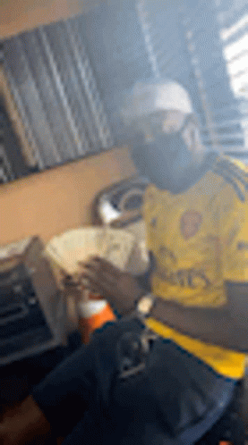 A Man In A Yellow Shirt Is Smoking A Cigarette While Holding A Bunch Of Money . GIF