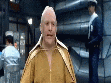 A Man In A Yellow Shirt Is Standing In A Room With A Police Officer Behind Him . GIF