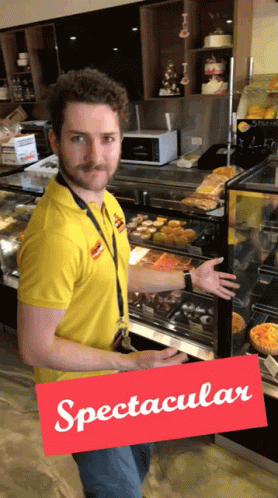 A Man In A Yellow Shirt Is Standing In Front Of A Display Case And A Sign That Says Spectacular GIF