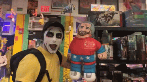 A Man In A Yellow Shirt Is Standing Next To A Stuffed Wrestler GIF