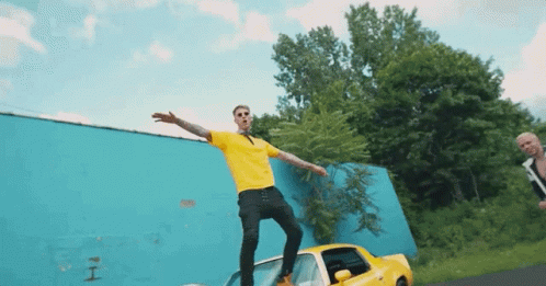 A Man In A Yellow Shirt Is Standing On A Car GIF