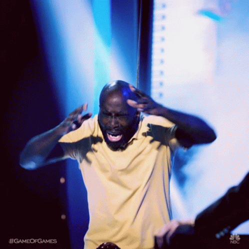 A Man In A Yellow Shirt Is Standing On A Stage With His Mouth Open GIF