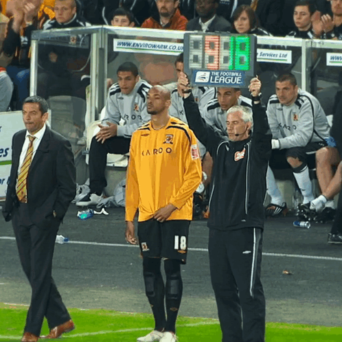 A Man In A Yellow Shirt With The Number 18 On It Stands On A Soccer Field GIF