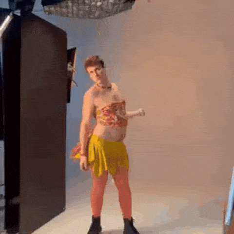 A Man In A Yellow Skirt And Top Is Standing In A Room . GIF