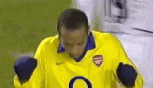 A Man In A Yellow Soccer Jersey Is Standing On A Field With His Hands In The Air . GIF
