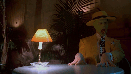 A Man In A Yellow Suit Is Sitting At A Table With A Lamp On It GIF
