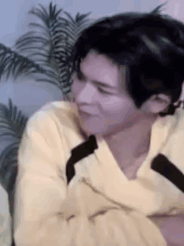 A Man In A Yellow Sweater Is Sitting In Front Of A Palm Tree And Making A Funny Face . GIF