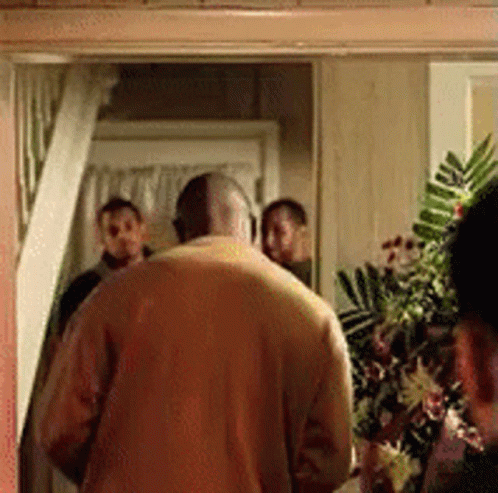 A Man In A Yellow Sweater Is Standing In A Doorway With A Group Of People Behind Him . GIF