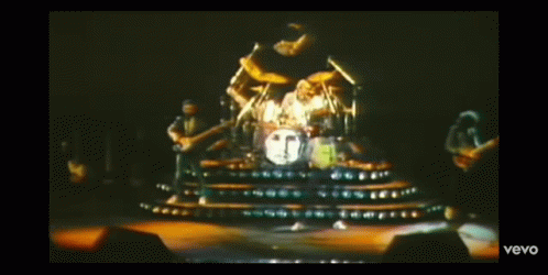 A Man In A Yellow Tank Top Is Playing Drums In A Video That Says Vevo On The Bottom Right GIF