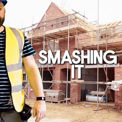 A Man In A Yellow Vest Stands In Front Of A Building Under Construction With The Words Smashing It Behind Him GIF