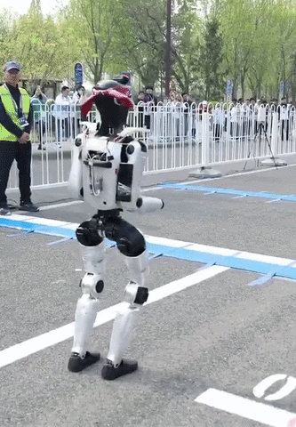 a man in a yellow vest stands next to a robot on the street