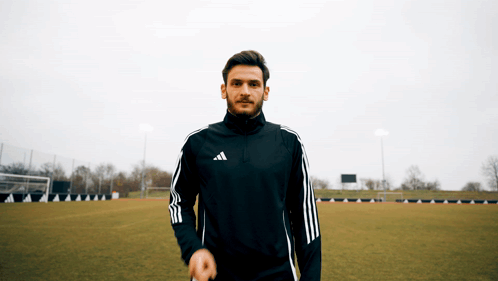 A Man In An Adidas Jacket Stands On A Field GIF
